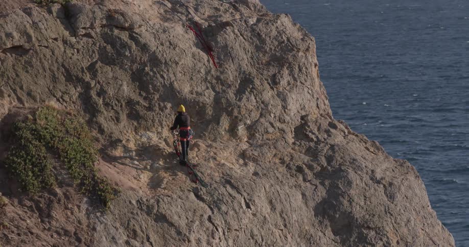Man stands on side of cliff untangling a harness