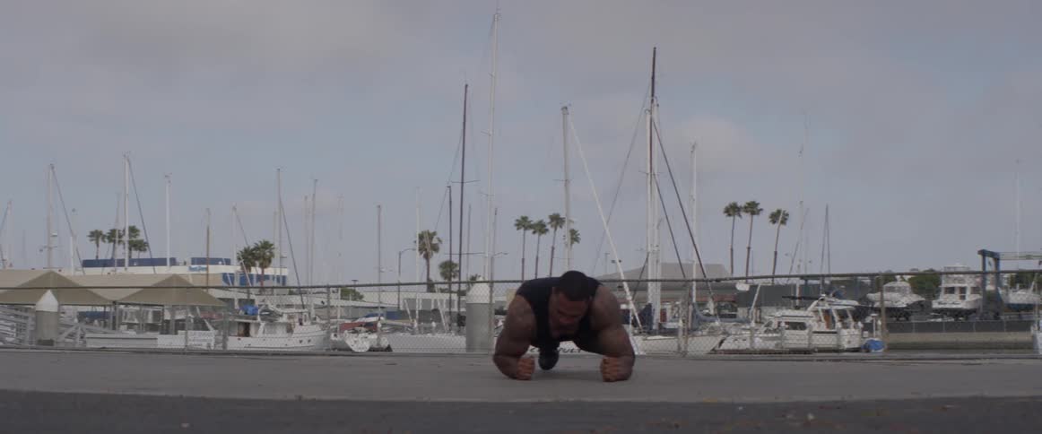 A man doing jumping push ups outdoors next to boats