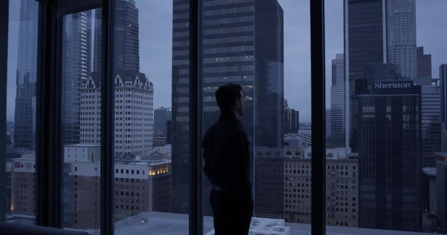 A man looks out a high rise window at the cities skyline
