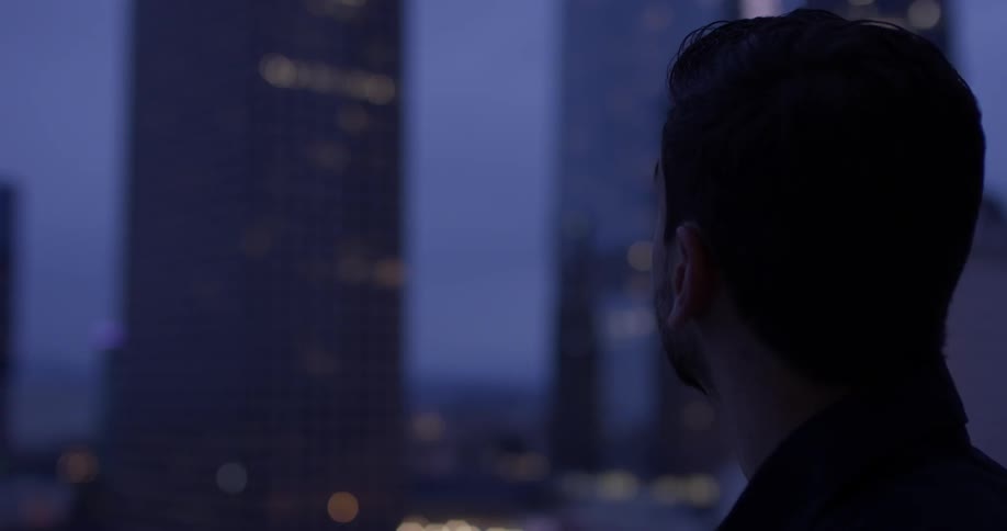 A man stares out a window at a lit up city