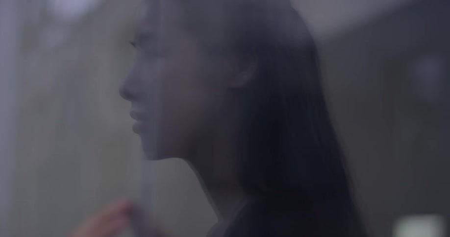 A woman swipes her hands along a piece of glass while dancing