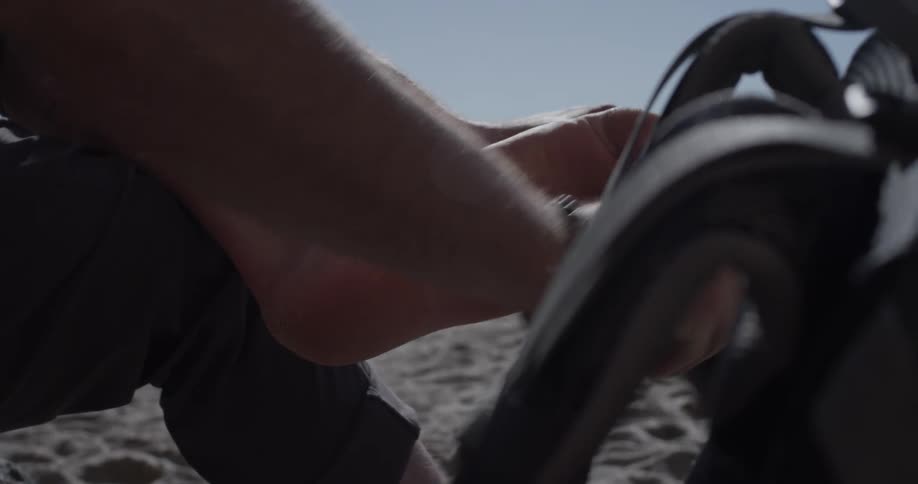 Man brushing sand off his foot and putting shoe on by the beach