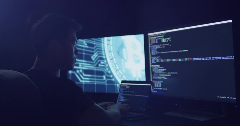 Man types on a laptop sitting in front of two monitors