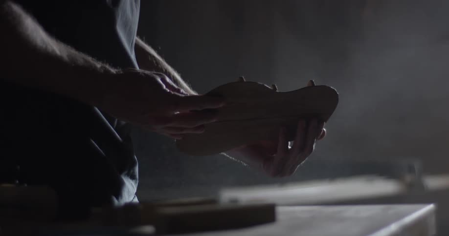 A man is inspecting a part for an acoustic guitar inside his workshop over his work table