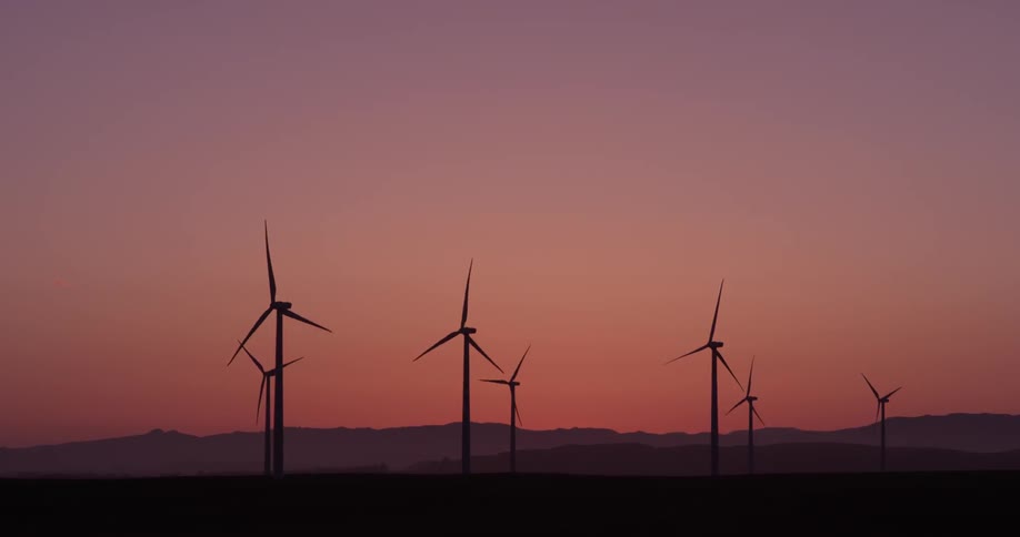 The sun sets in the distance as turbines spin collecting energy