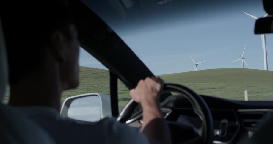 Man Driving Electric Car Through Wind Farm