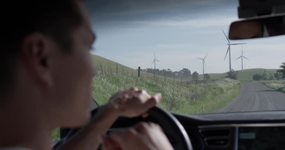 A man driving a car with one hand down a dirt road