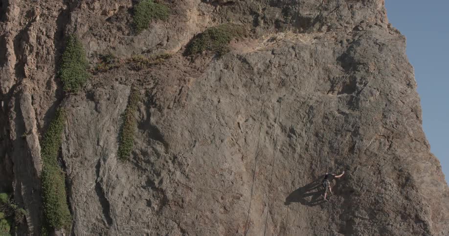 Man scales the side of a tall rocky cliff