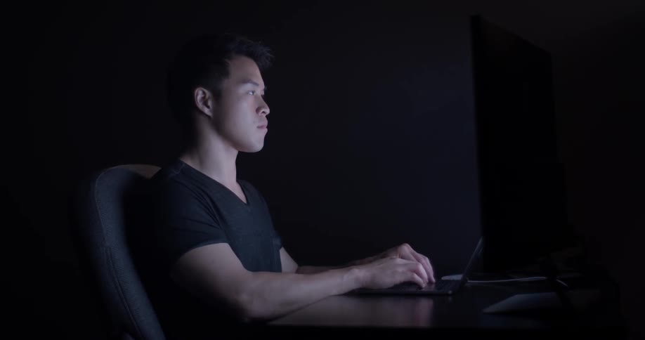 A man looks up and down between a laptop and monitors