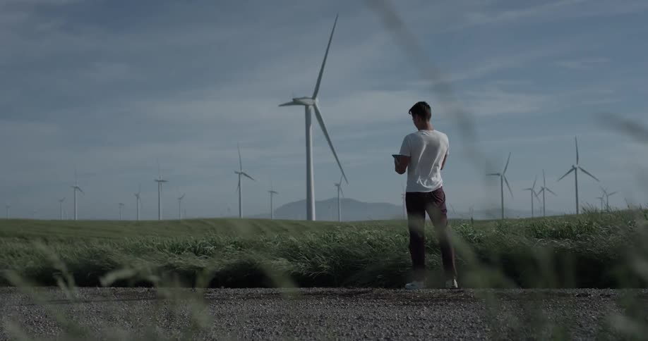 A man stands before a field of windmills