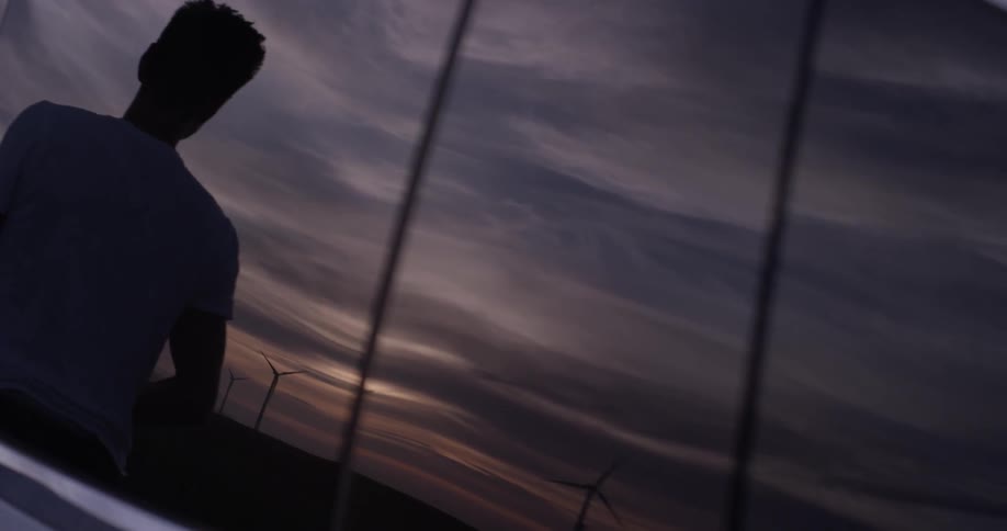 The reflection of a man getting out of a car during a sunset near windmills