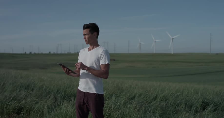 A man that is using a tablet out in the middle of a field
