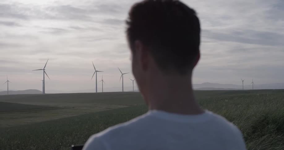 Man uses a tablet while watching windmills at a wind farm