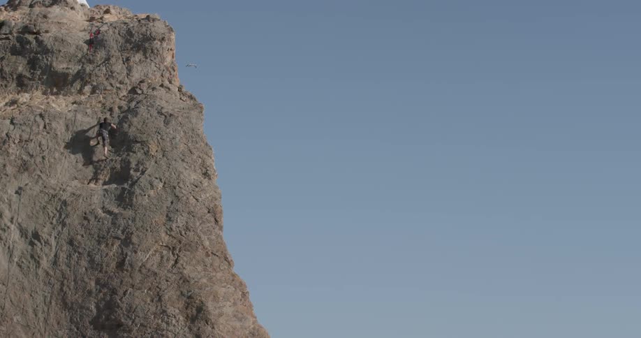A man can be seen off in the distance scaling a mountain with his rock climbing equipment