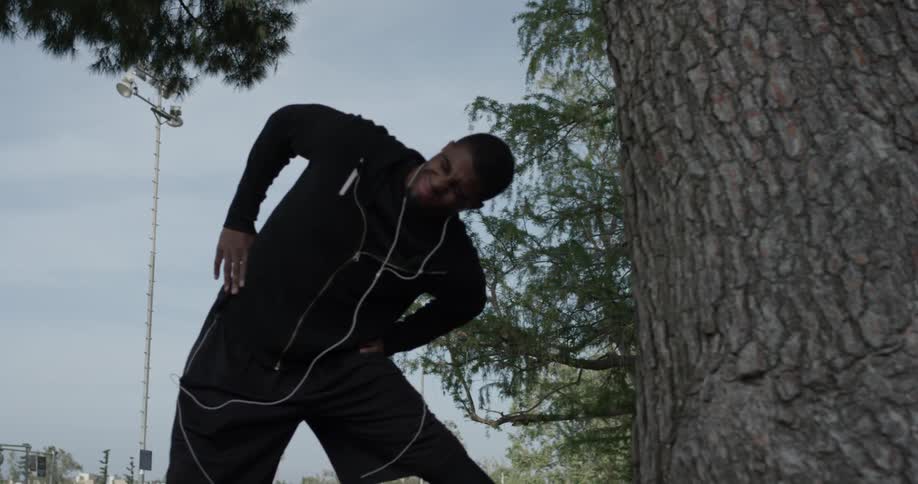 A man that is stretching outdoors next to a tree
