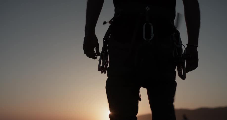 A man wearing a harness standing up at the top of a mountain
