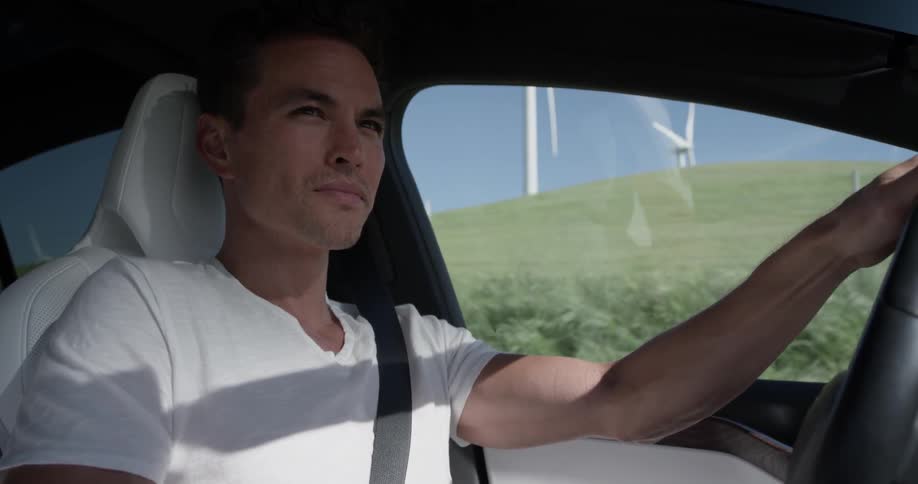 A man driving a car through a field that has windmills in it