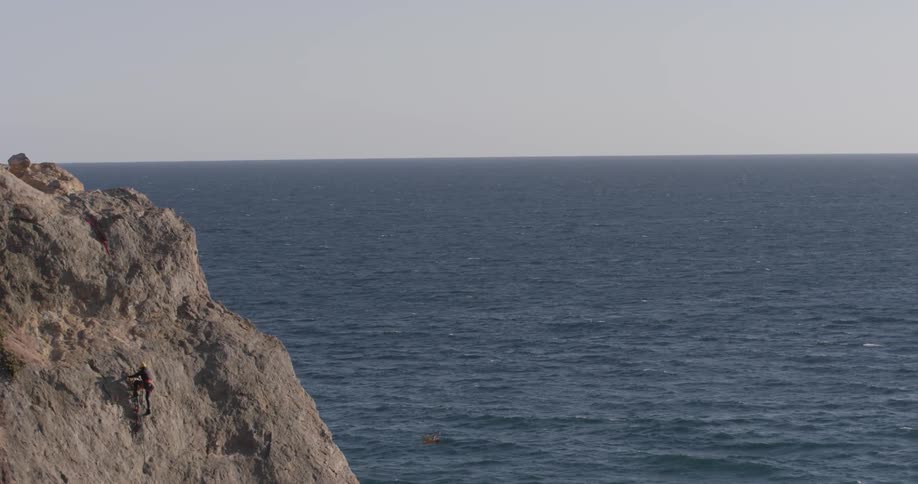 A man that is climbing up a mountain next to the ocean