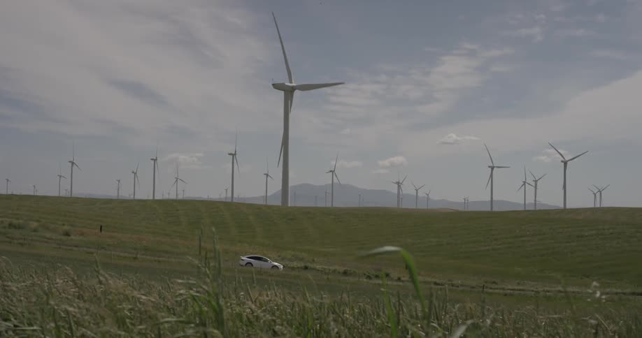 Man Driving Electric Car Through Wind Farm