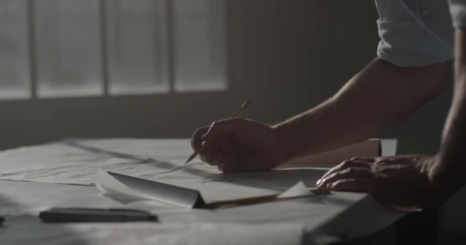 Person writes on blueprints on a table with a pencil
