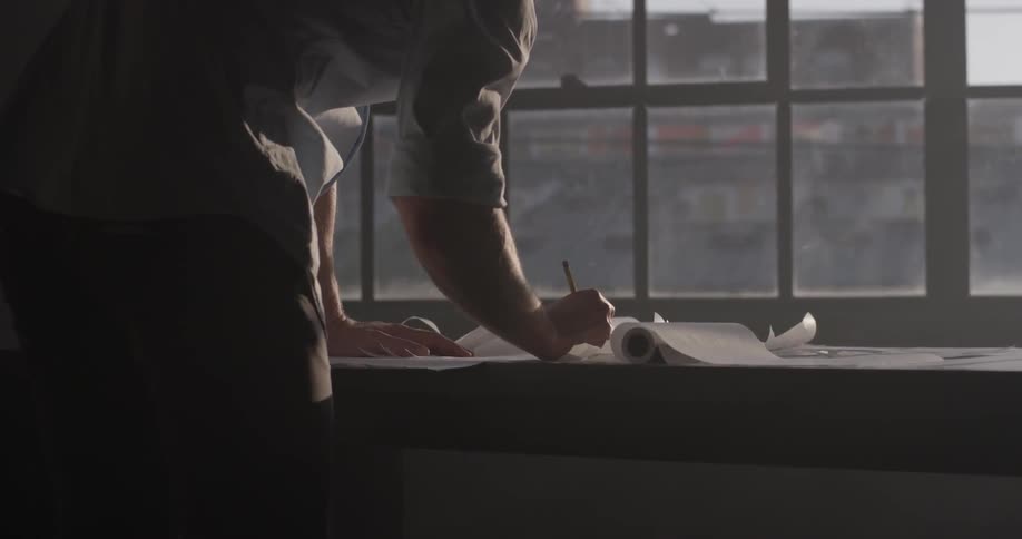 Man standing at a table draws with pencil on rolls of paper