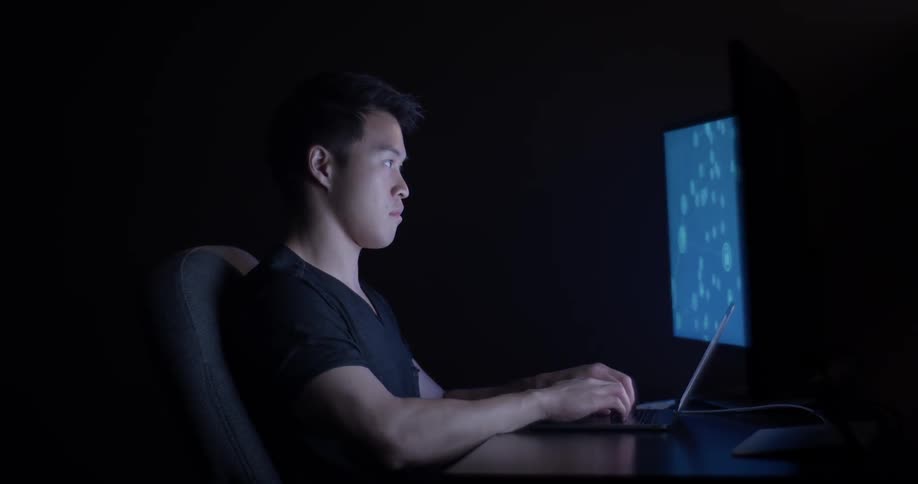 A man is looking at a laptop and typing on it