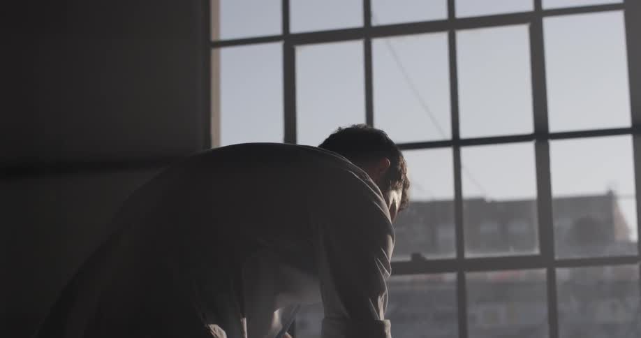 A man leaning on a table writing by large windows