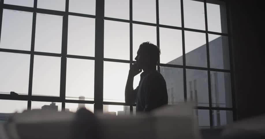 A man looking out a window talking on a phone