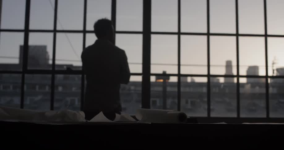 A man standing by a large window looking out to the city