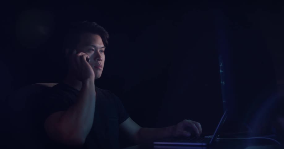 Man sits at desk with multiple monitors and answers a cell phone