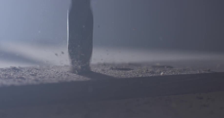 Drilling into a piece of wood in a dim lit room with a spotlight