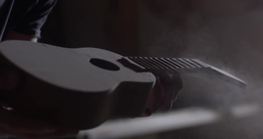 Person blows sawdust off an unfinished ukulele