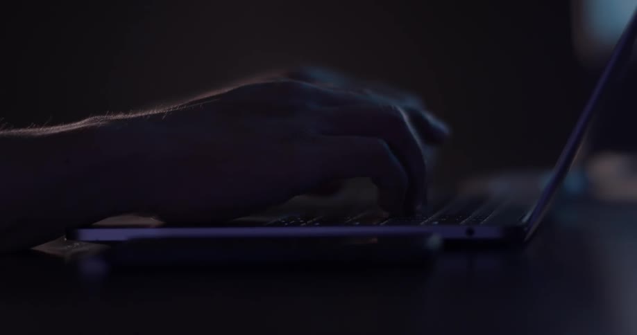 Man typing on a laptop in a dark office