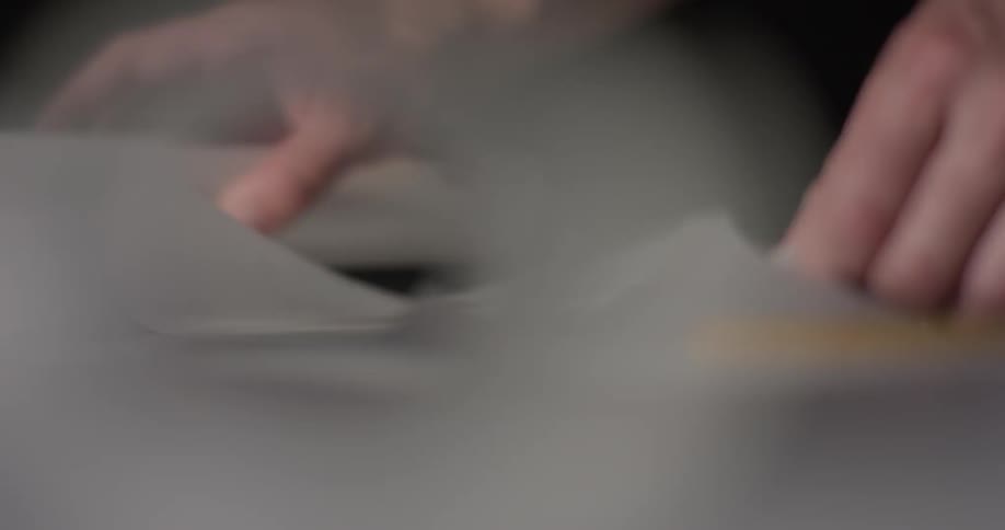 A person puts down a pencil and then uses an edge ruler to rip a piece of paper from the roll