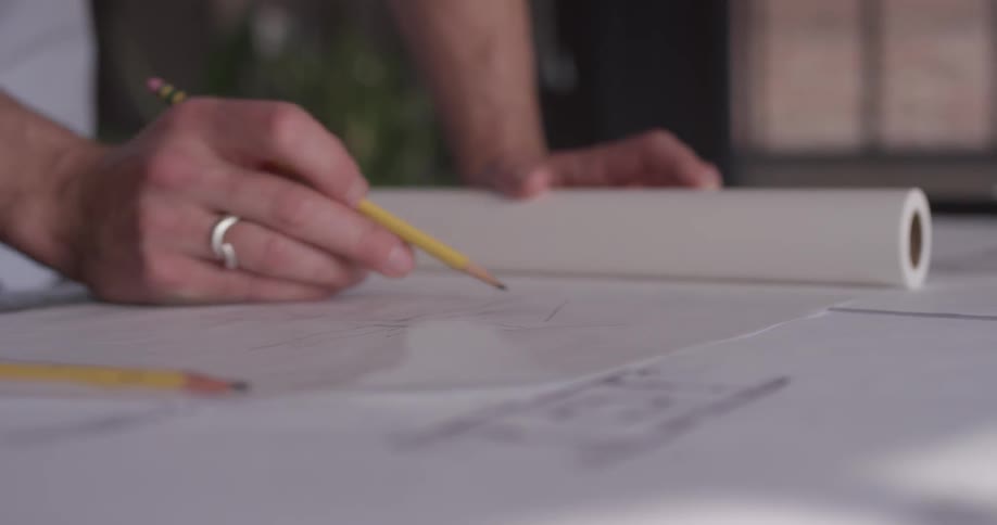 Man's hands are drawing on a piece of paper with a pencil