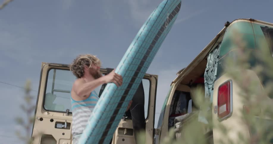 A man in a striped shirt pulls his surfboard out of a van