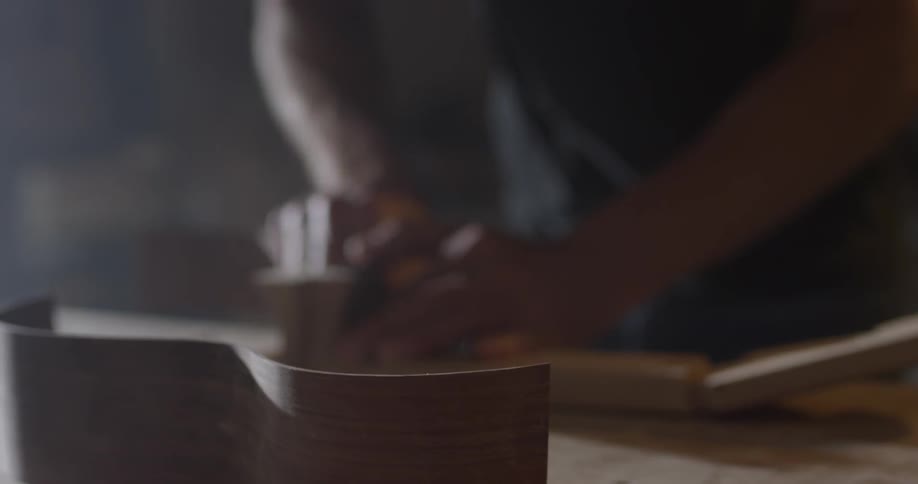 A man works at his work bench in his workshop creating the side part for an acoustic guitar