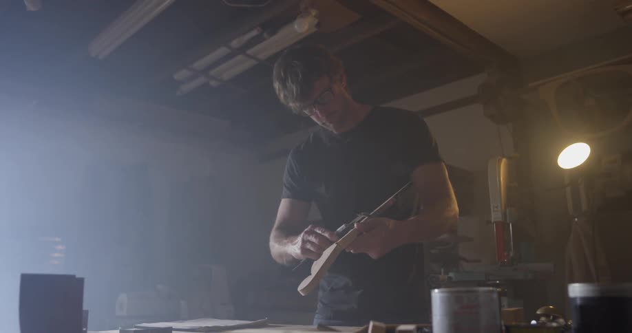 A man uses a tool to measure an incomplete ukulele he is making