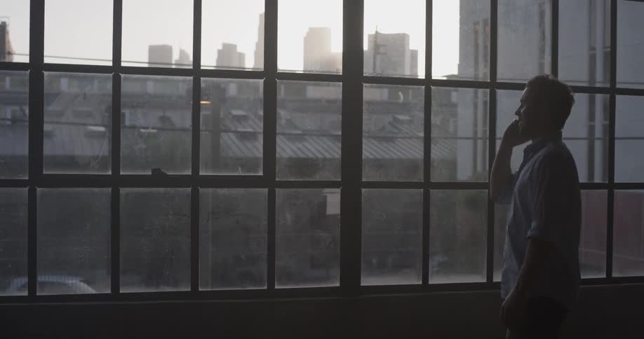 A man talking on a cell phone in front of a window