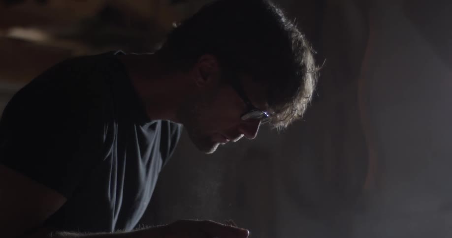 A man that is blowing sawdust off of a piece of wood