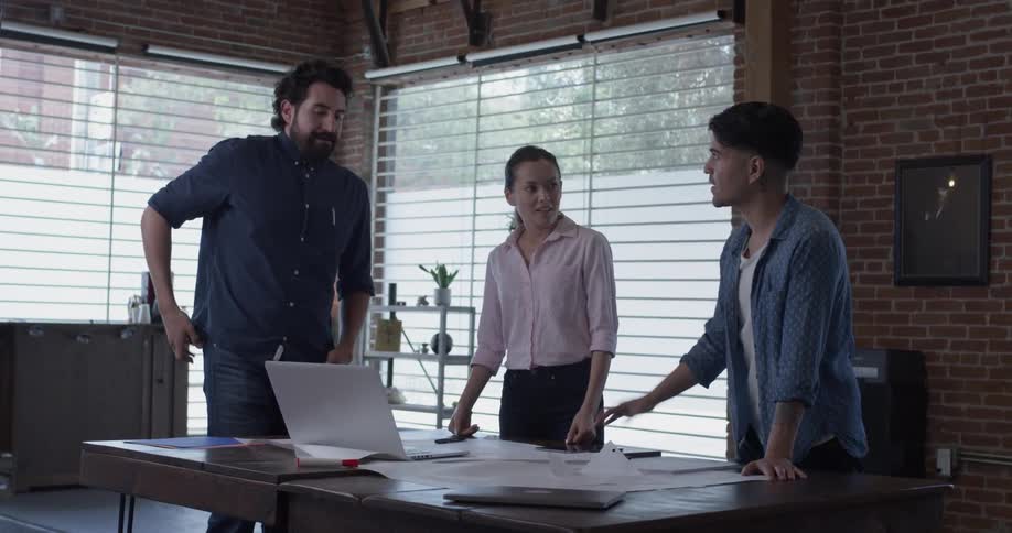 Two men and a woman stand around a table talking business