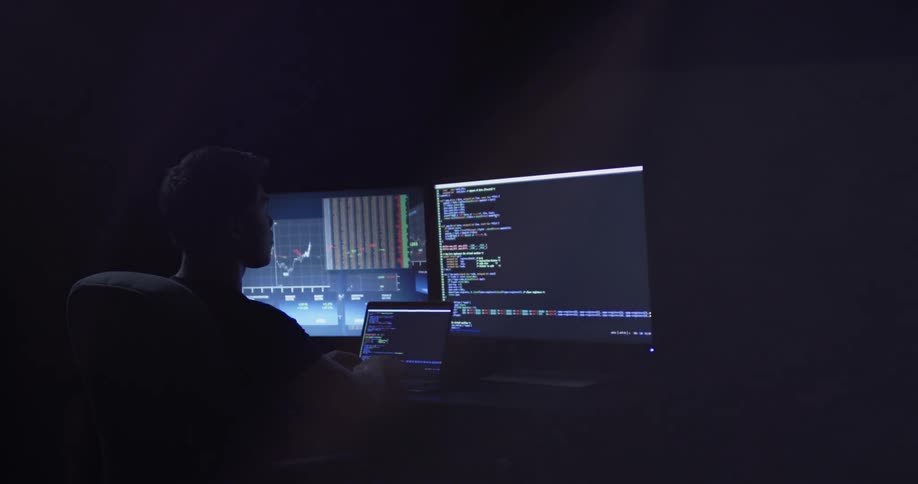 A man sitting in an office looking at 3 computer screens