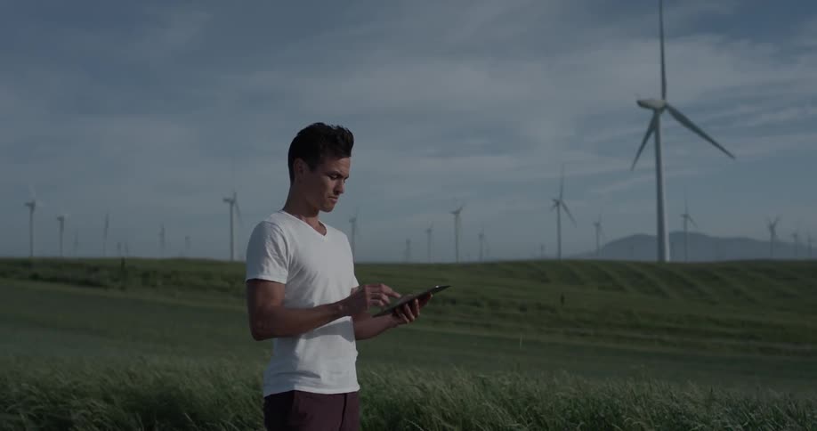 A man stands in a green field with many windmills on a tablet