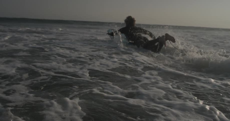 A surfer jumps onto his board and paddles out into the ocean