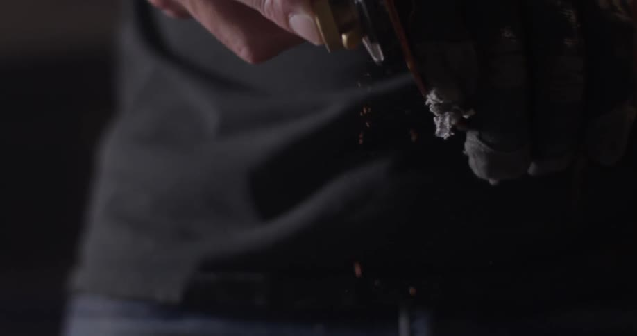 A man sands a piece of wood in a dark room