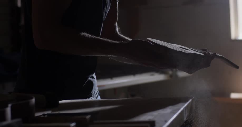 A man picks up a ukulele and brushes then blows dust off of it