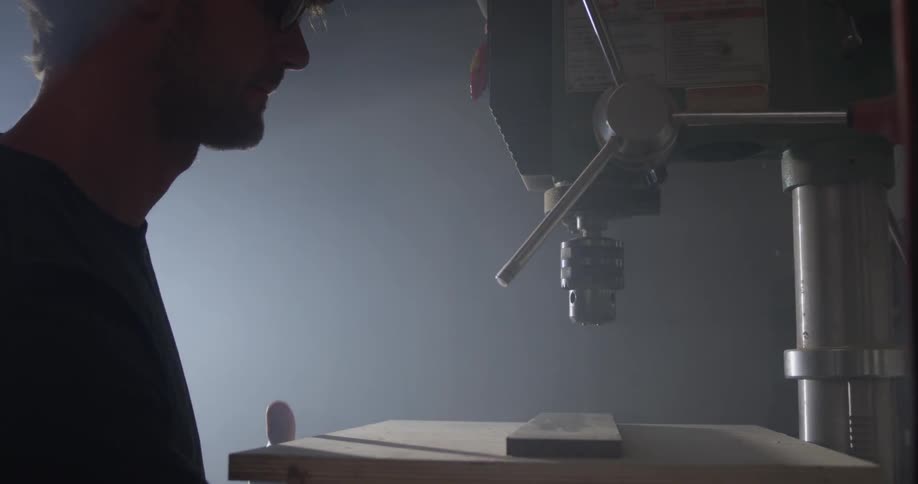 A man walks up to use a drill press as light shines on him from a window