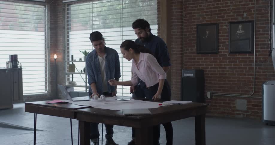 Woman draws on white paper on table and explains something to colleagues