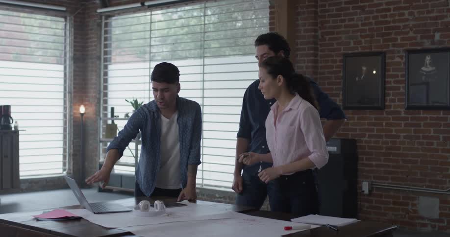 Three people working together on a design on paper and a computer