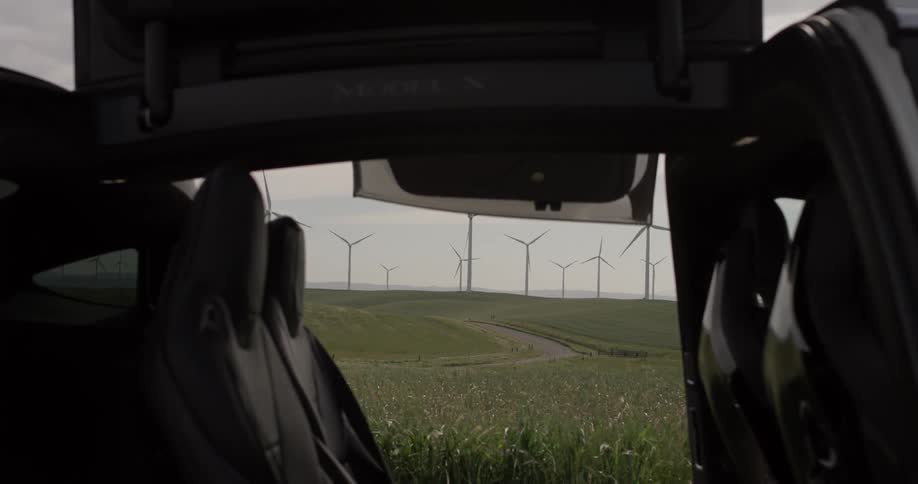 A car door opening to reveal a grassy field with windmills